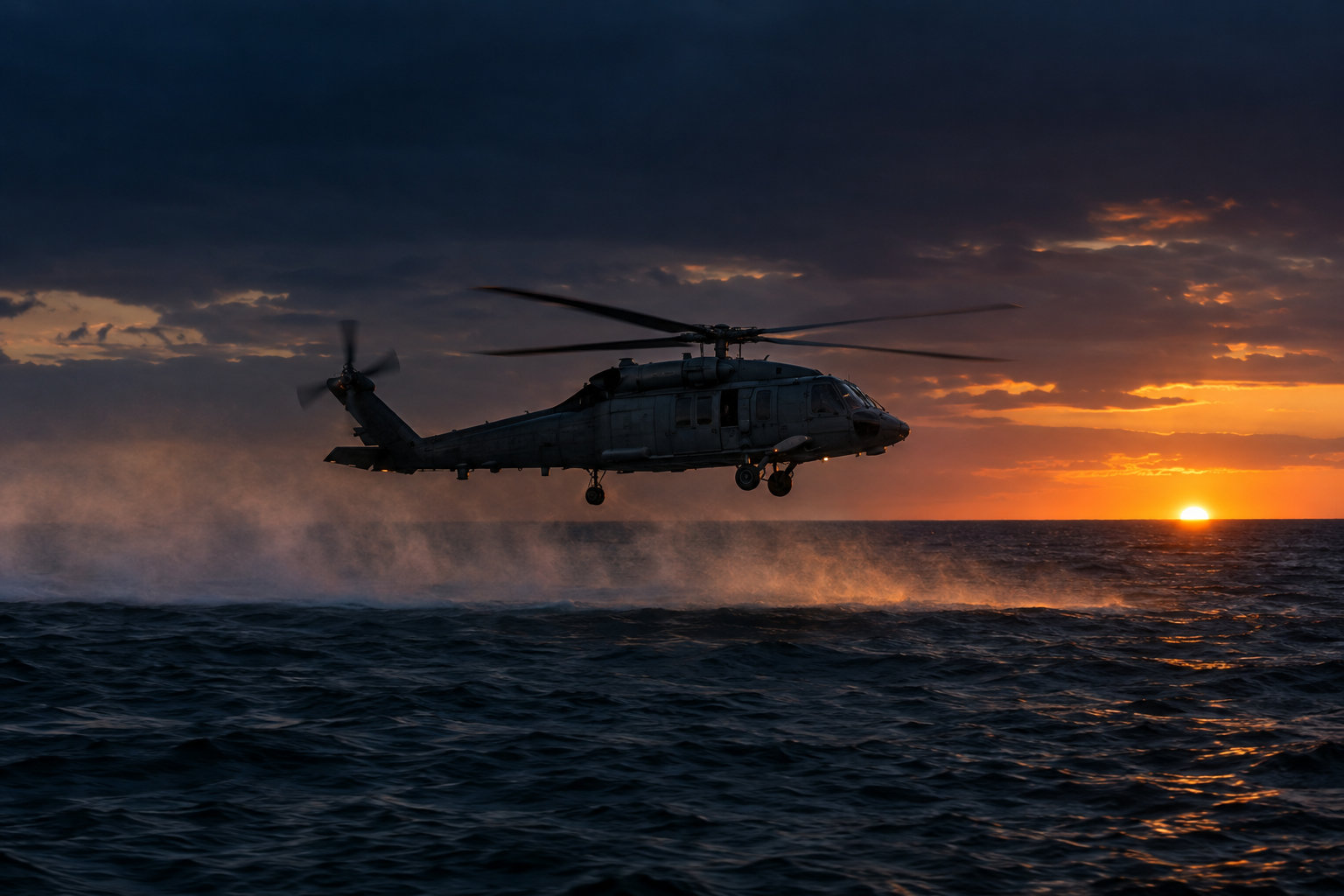A Navy helicopter flying low over open ocean at dusk